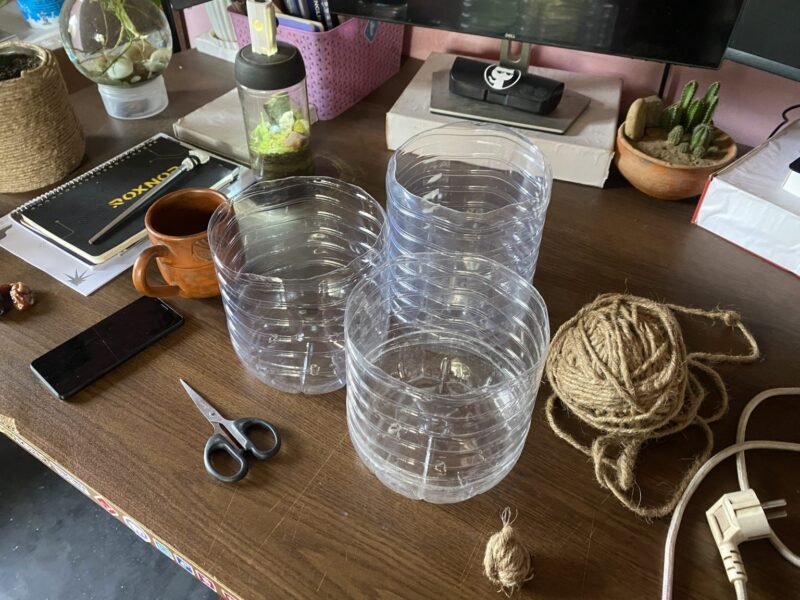 A wooden desk with containers, scissors, a phone, a mug, a notebook, and plants.