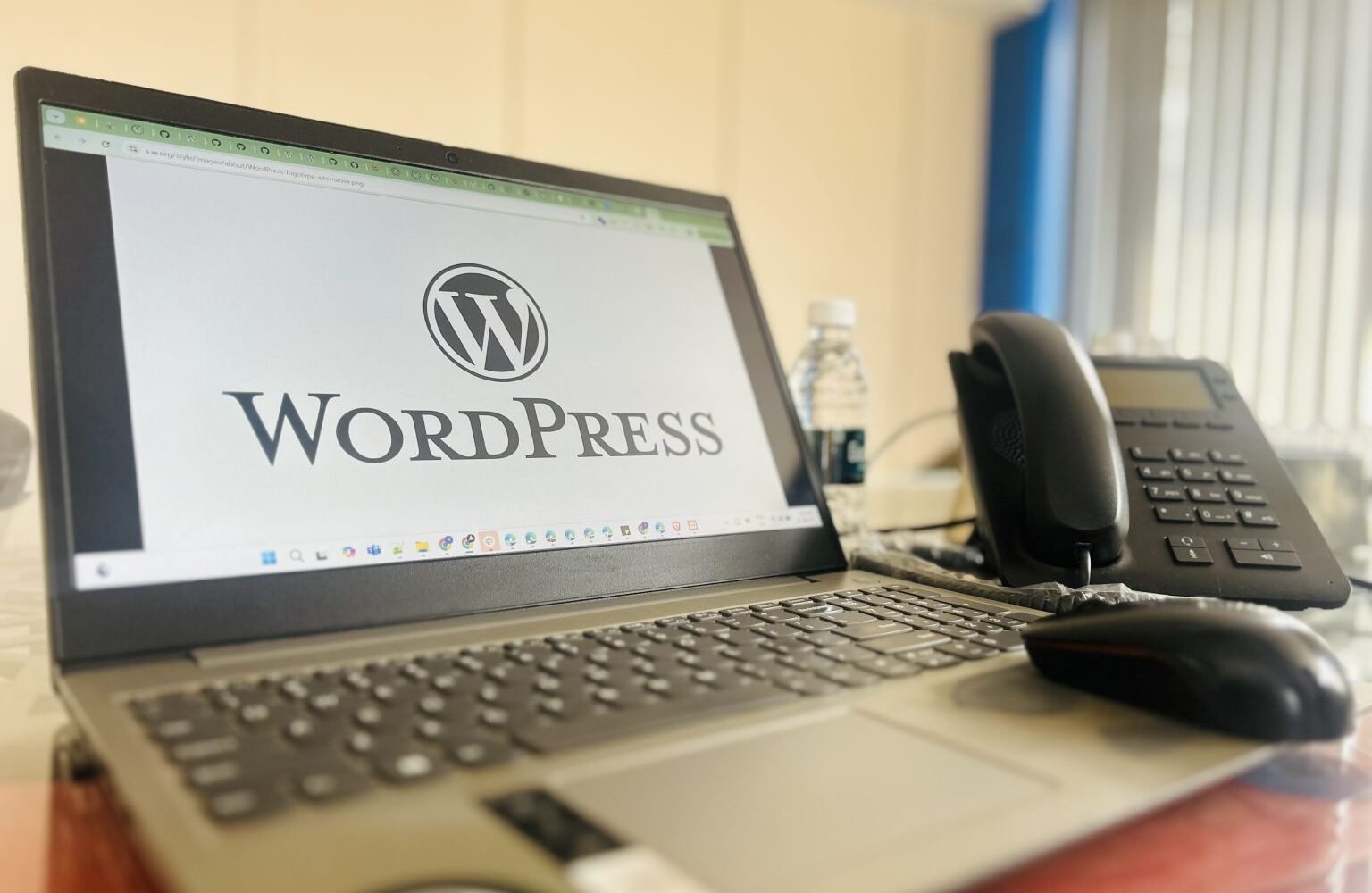 Laptop displaying WordPress on an office desk with a smartphone and desk phone.