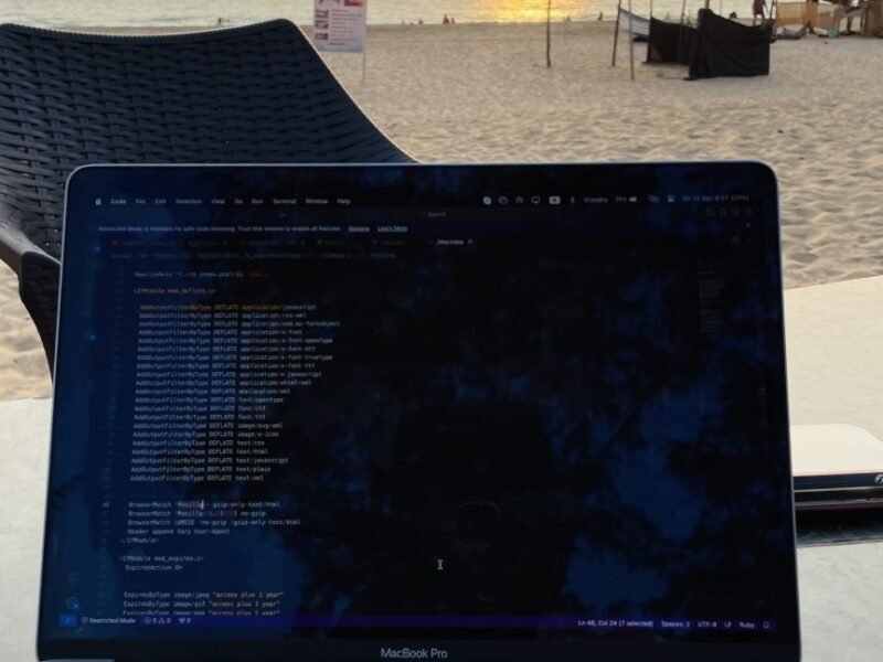 A laptop on a table with code on screen beside a beach at sunset.